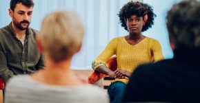 Diverse group of patients gathered in circle at psychologist office discussing self problems while listening others. Getting psychological support. Focus on an african american woman with afro hair.