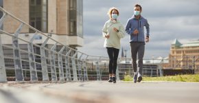 Young couple wearing protective masks jogging together in the morning along the street