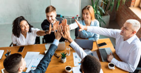 Teamwork. Happy Coworkers Giving High-Five Celebrating Business Success Sitting Together At One Desk In Modern Office.