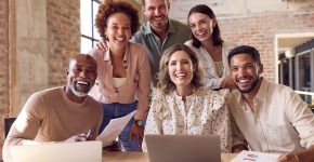 Portrait Of Multi-Cultural Business Team Meeting Around Laptop In Busy Office