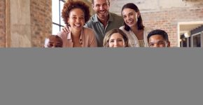 Portrait Of Multi-Cultural Business Team Meeting Around Laptop In Busy Office